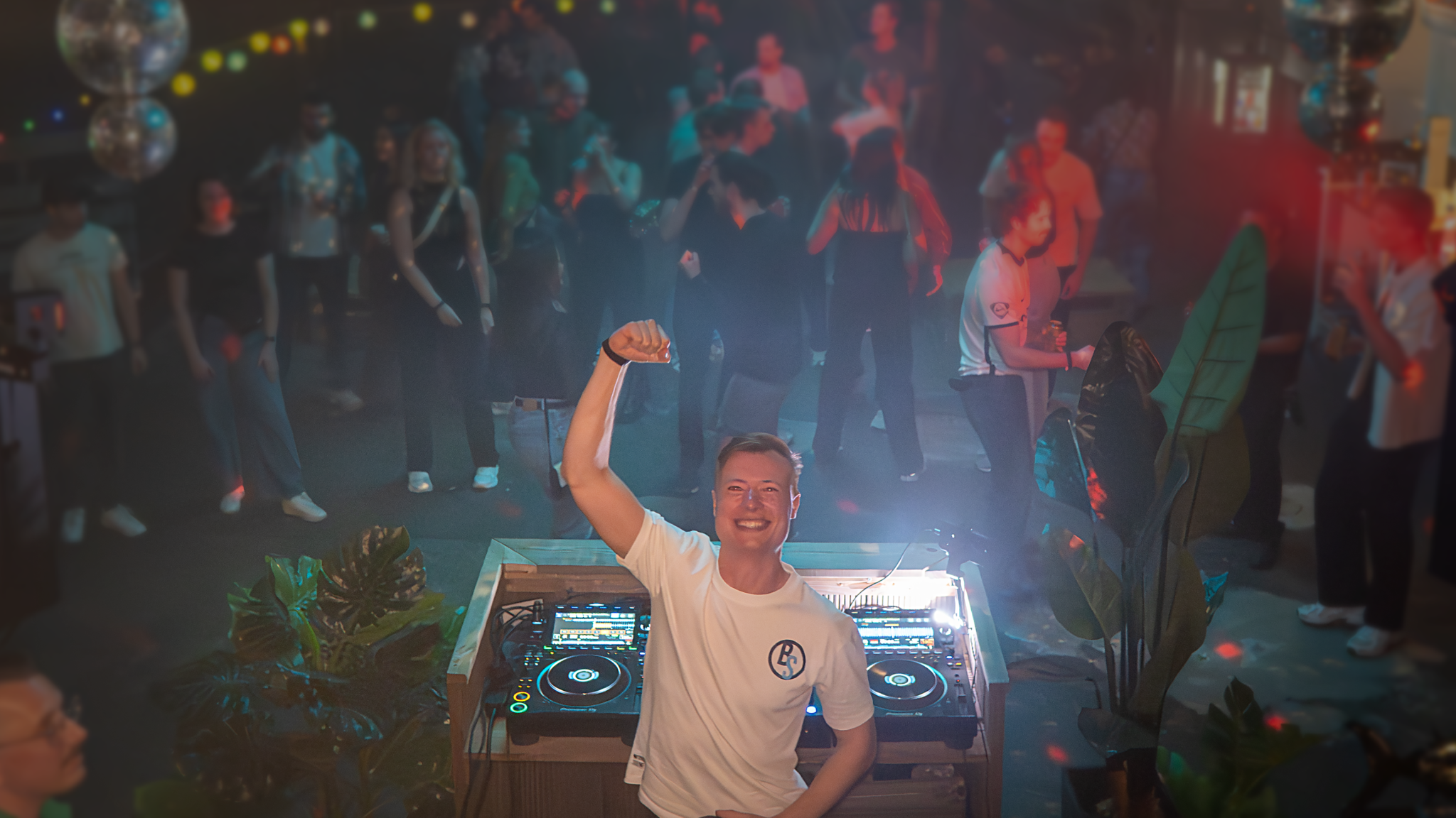 PresidentBrie performing an indoor tech house DJ set at Shake Je Container, delivering driving grooves as the crowd dances in a packed venue.”